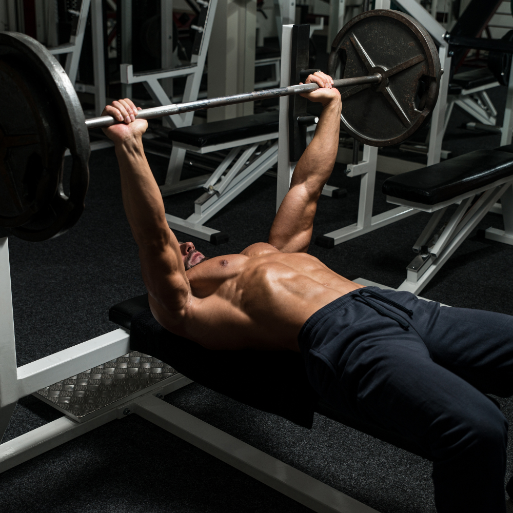 Man performing a bench press with a barbell in a gym setting
