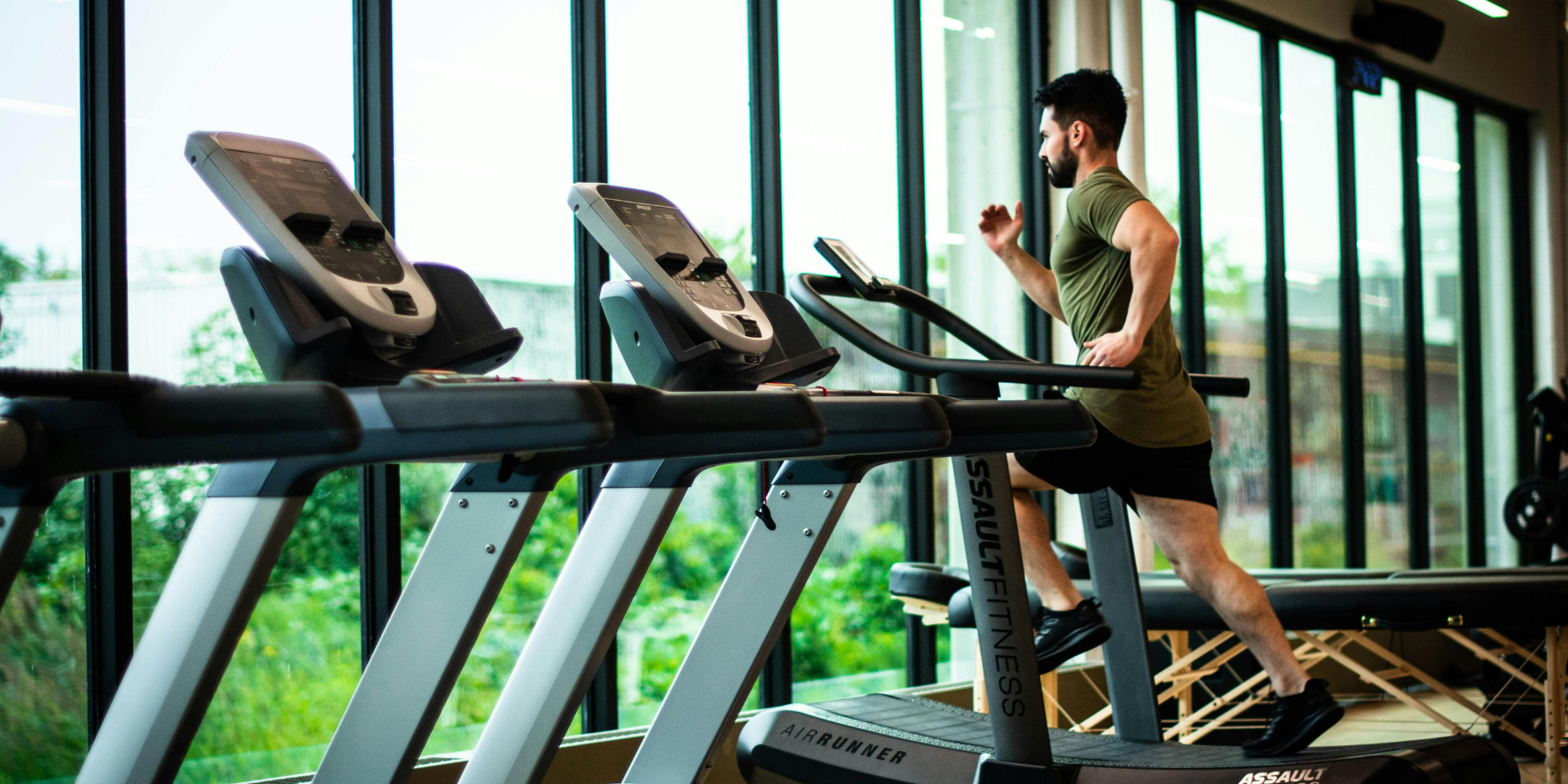 Man running on a treadmill in a gym with large windows