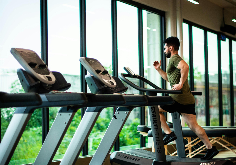 Person running on a treadmill in a gym with large windows